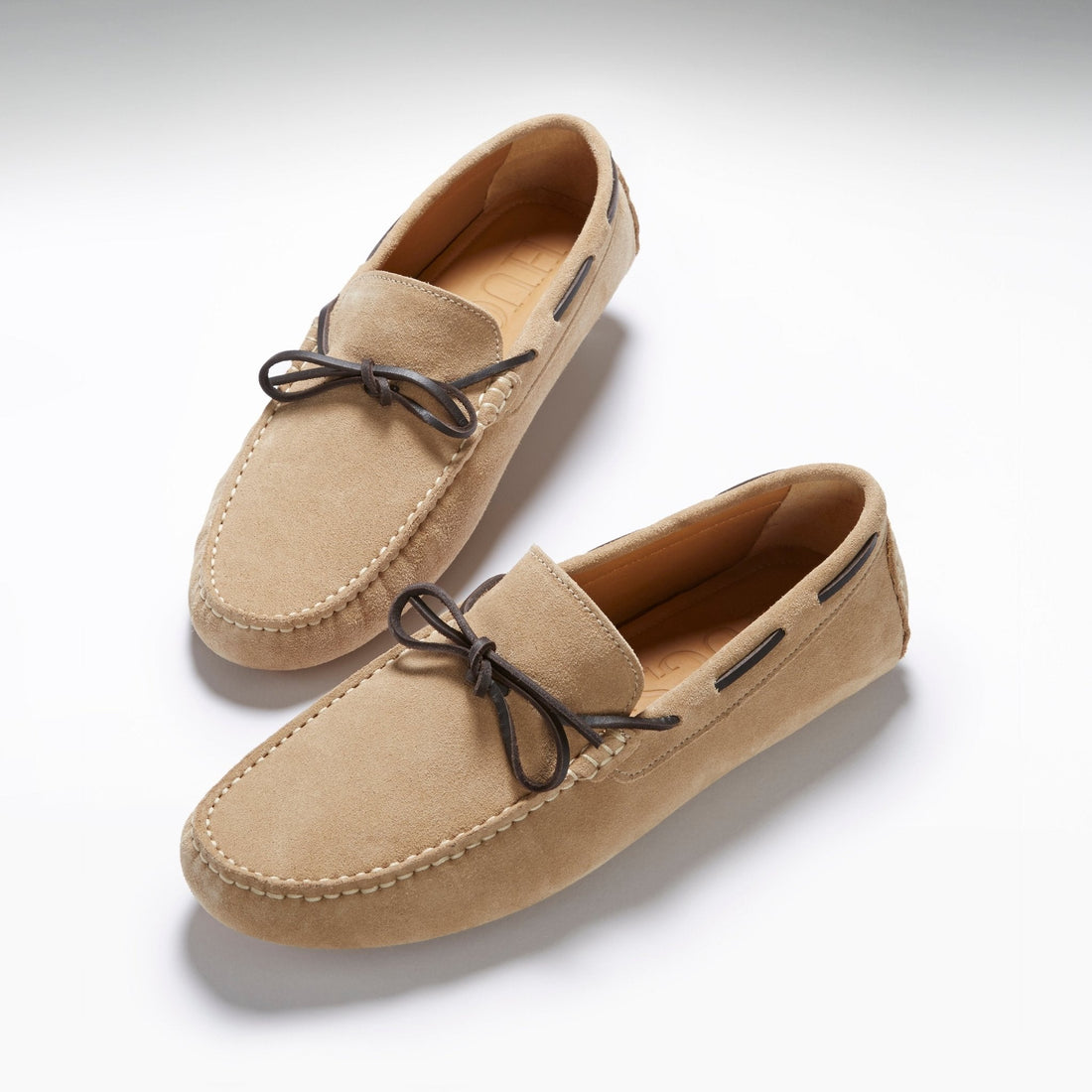 Pair of taupe suede driving loafers with dark bow laces and moc-toe stitching