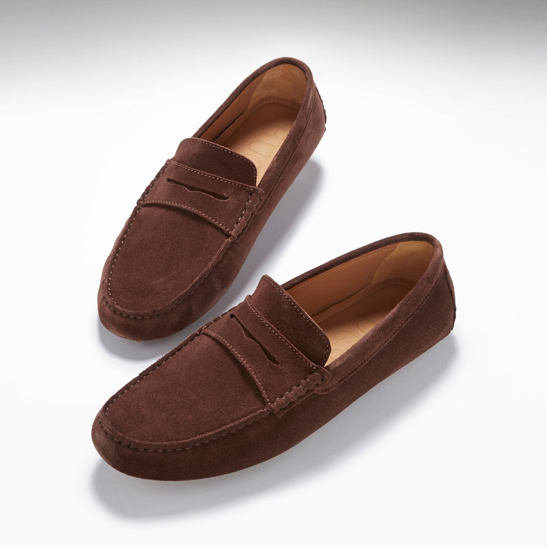 Pair of brown suede penny loafers with tan lining and stitched apron toes