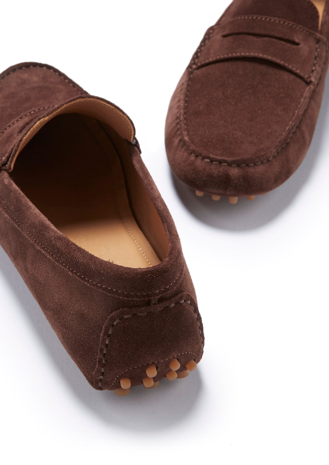 Brown suede driving loafers showing stitched heel panels and rubber sole pods