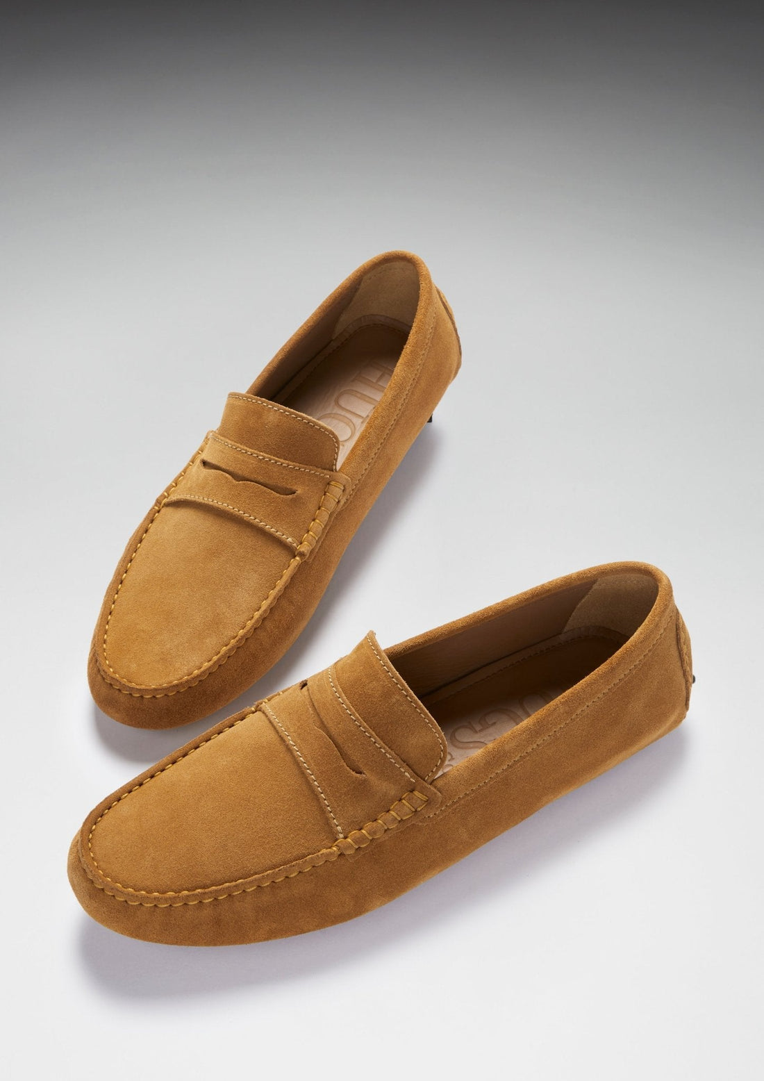 Pair of tan suede penny driving loafers, shown at an angle with stitched apron toes.