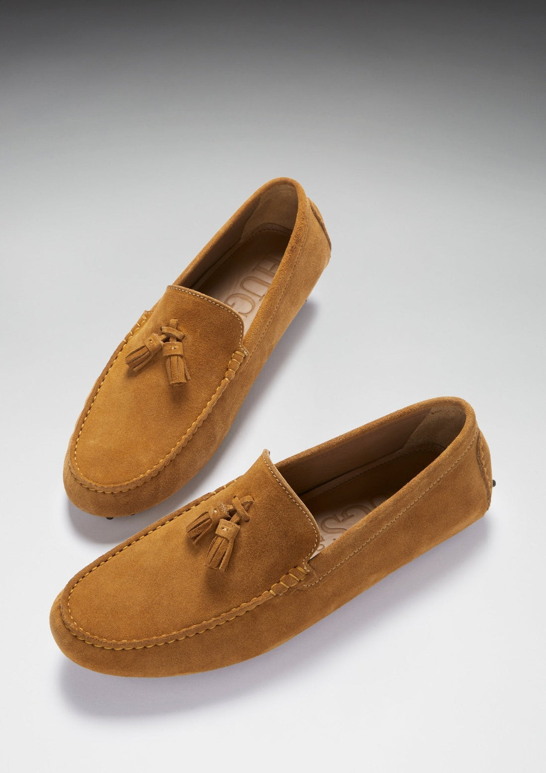 Pair of tan suede driving loafers with tassels and stitched moc toes, viewed at an angle