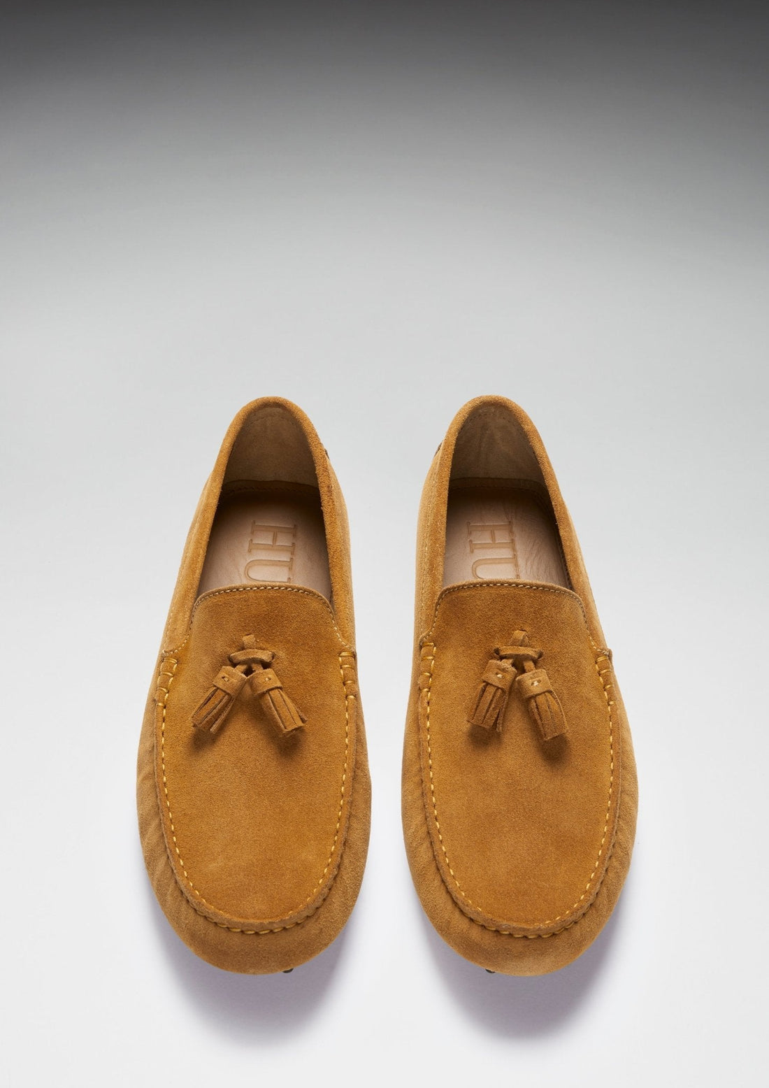 Pair of tan suede loafers shown from above, with tassels and stitched moc toes