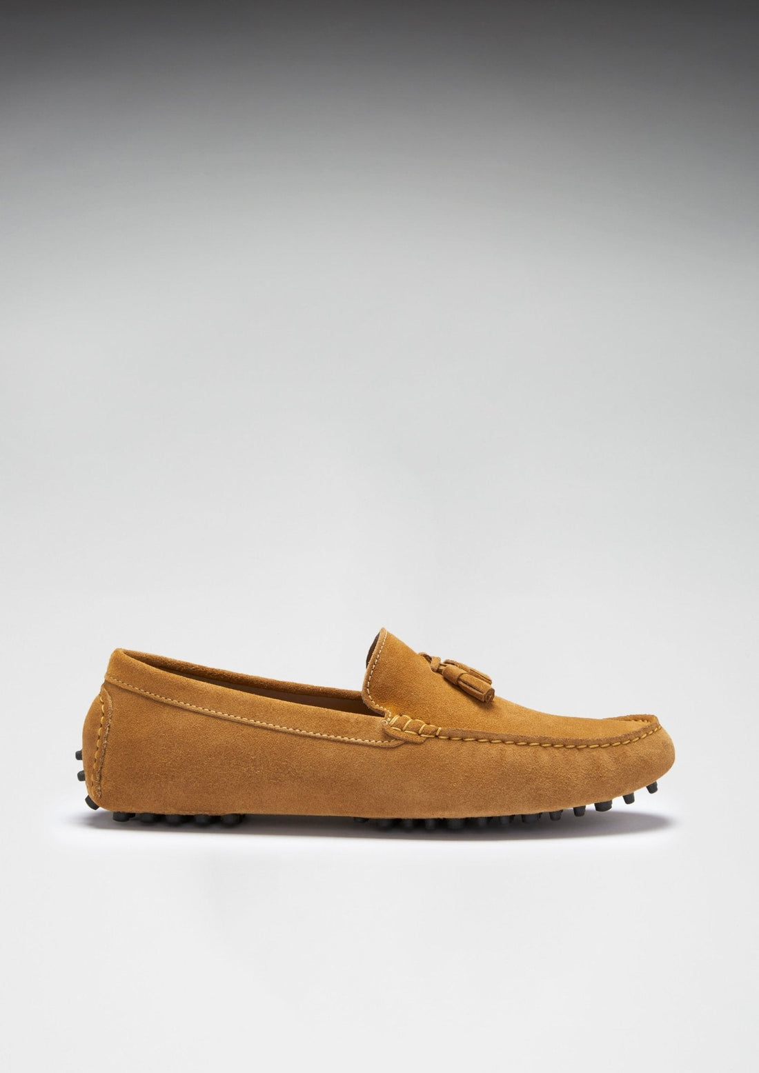 Side view of a tan suede driving loafer with tassel detail and rubber stud sole