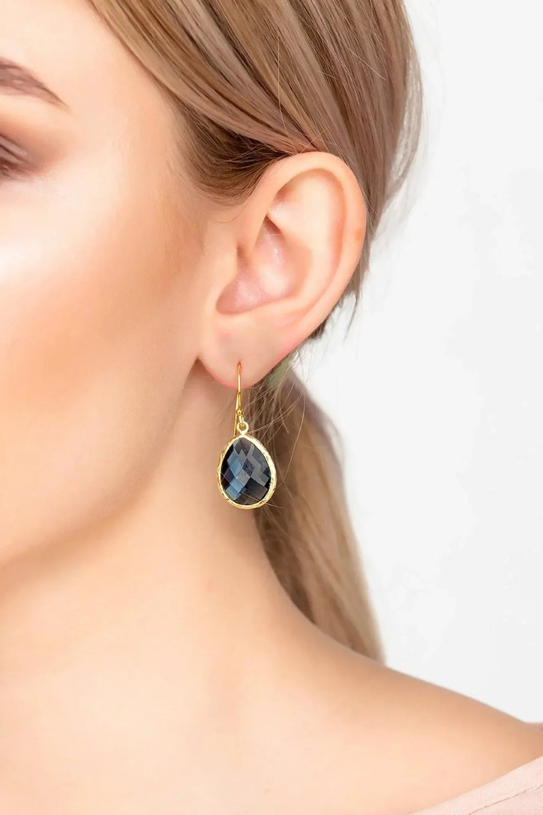 Gold drop earrings on model ear, dark blue teardrop faceted gemstone