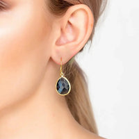 Gold drop earrings on model ear, dark blue teardrop faceted gemstone