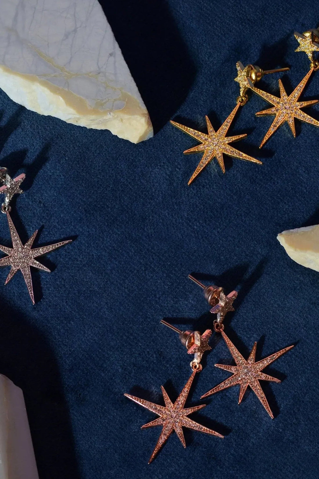 Gold starburst drop earrings with dangling star charms on dark fabric