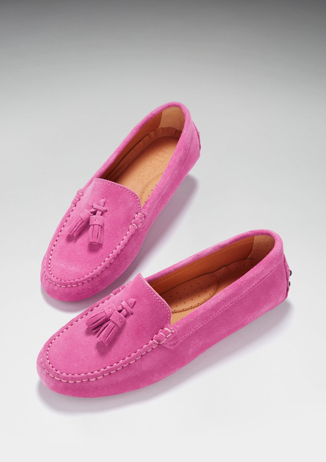 Pink suede tassel loafers shown at an angle, with stitched toes and tan lining.