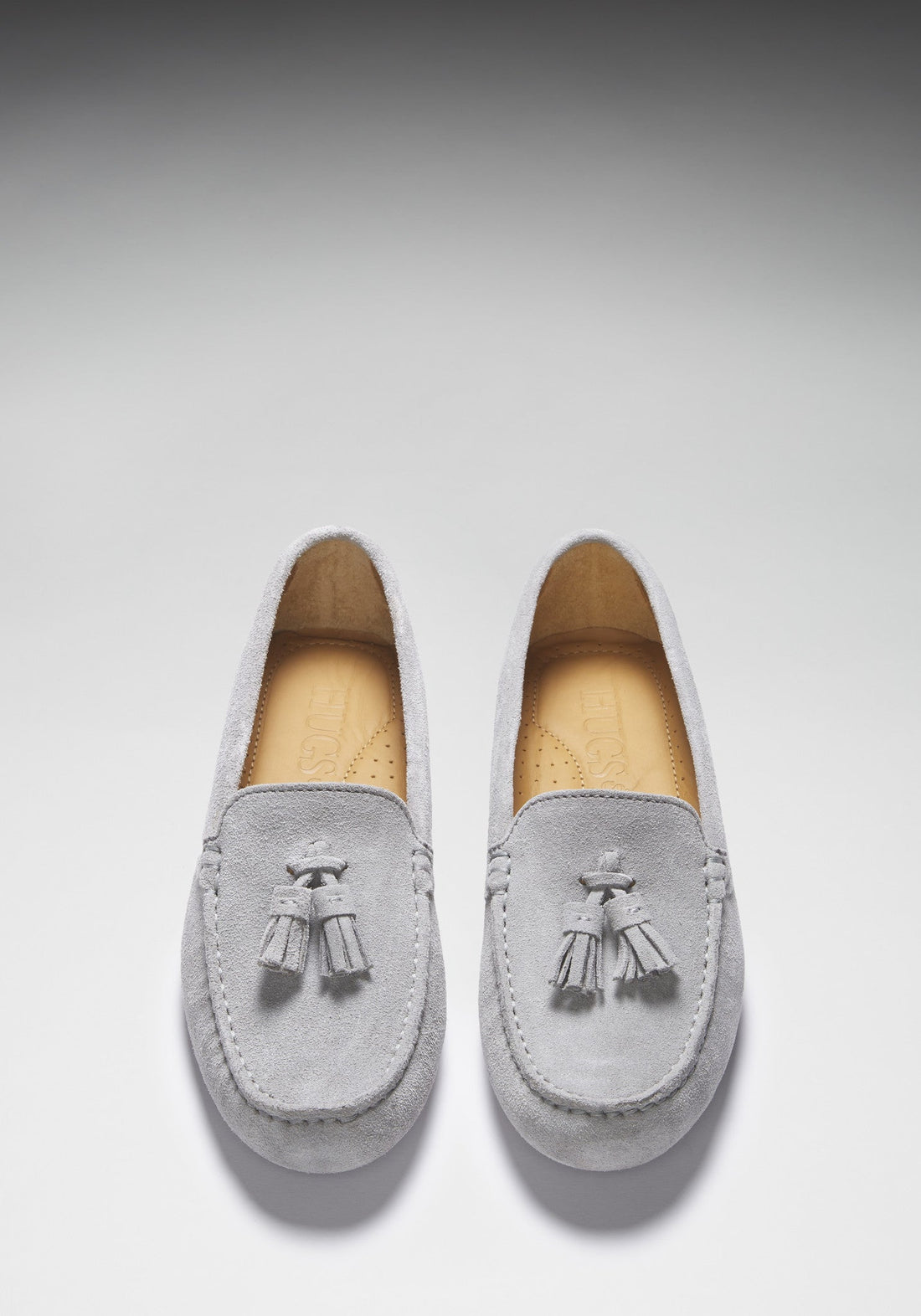 Top view of grey suede loafers with tassels and tan insoles.