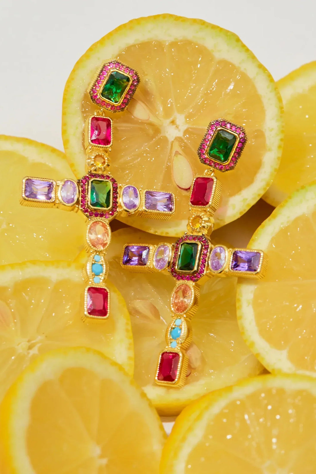 Gold cross gemstone earrings close-up with green red purple and blue stones
