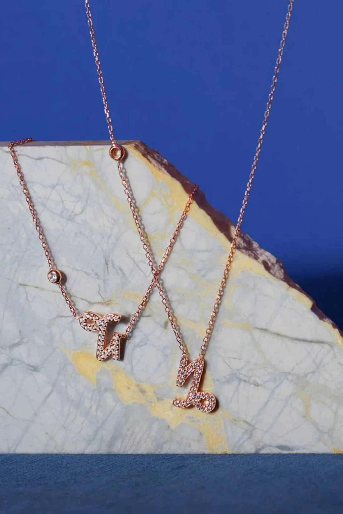Rose gold Capricorn charm pendant necklace on stone, multiple chains visible